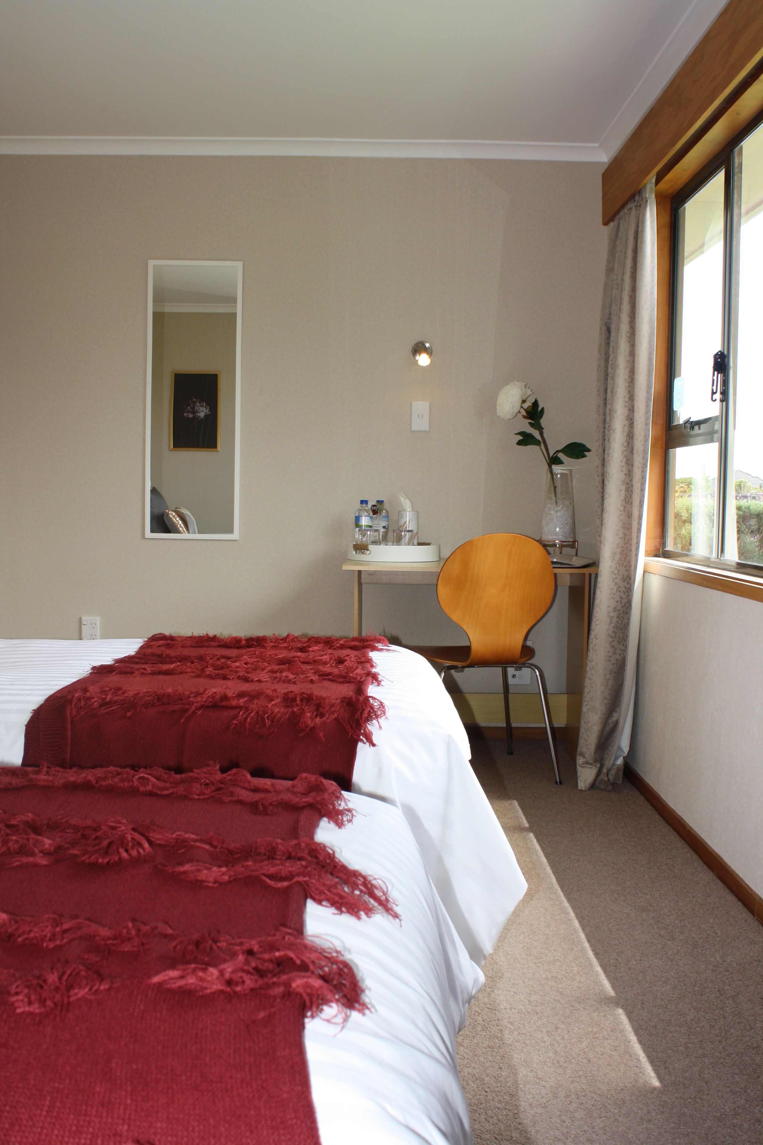 A hotel room with a bed, a desk, a chair, a mirror, and a window with curtains.