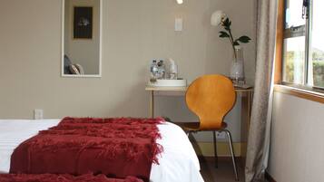 A hotel room with a bed, a desk, a chair, a mirror, and a window with curtains.