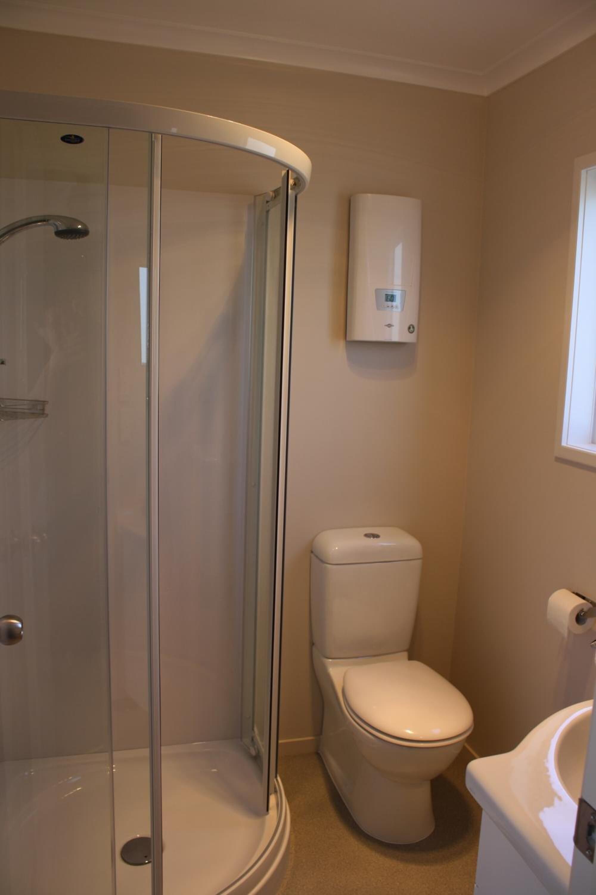 A bathroom with a glass-enclosed shower, a toilet, and a wall-mounted water heater.