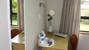 Habitación compacta con ducha, una mesita de noche con artículos de aseo, una silla y una ventana con cortinas.