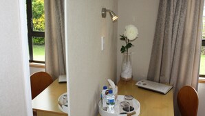 Una habitación con una mesa de madera, un florero con una flor blanca, una botella de agua, un vaso, un pañuelo de papel y una pequeña bandeja con un cuaderno y un bolígrafo.