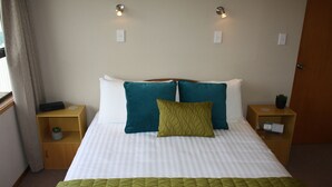 A neatly made bed with white and green bedding, two bedside tables with lamps, and a small plant on one of the tables. - Jenny's Bed & Breakfast (New Plymouth)