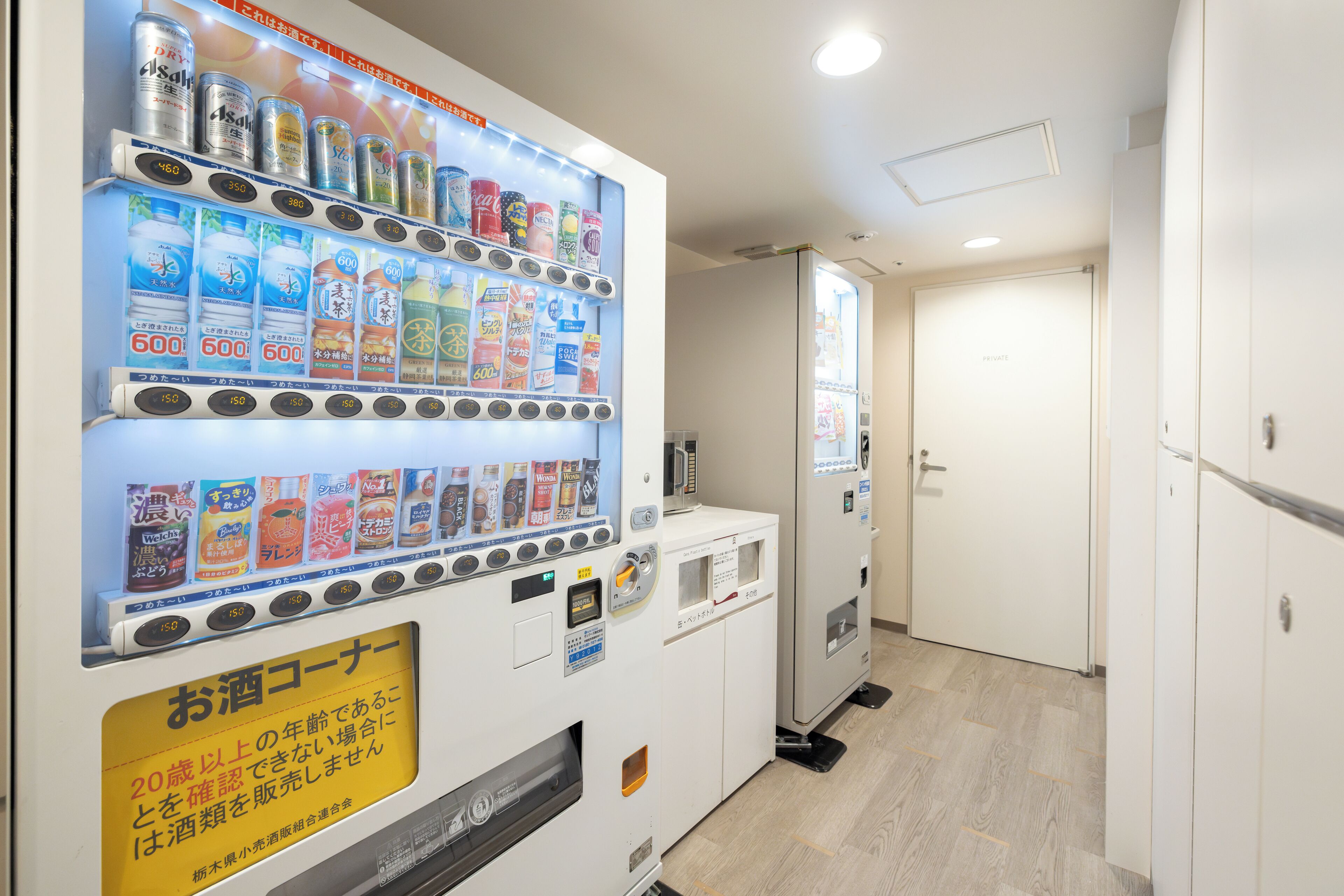 A vending machine with various drinks and snacks, a private door, and a wooden floor.