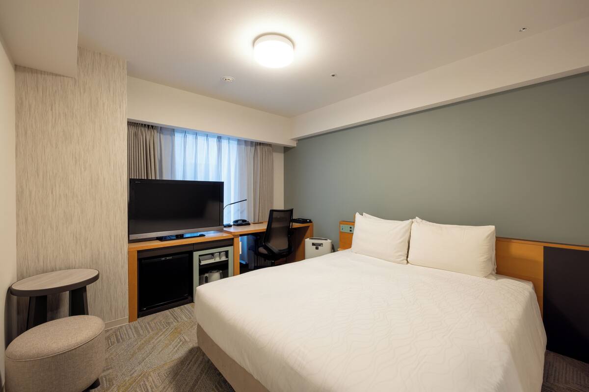 A hotel room with a large bed, a desk with a computer, a TV, and a small seating area.