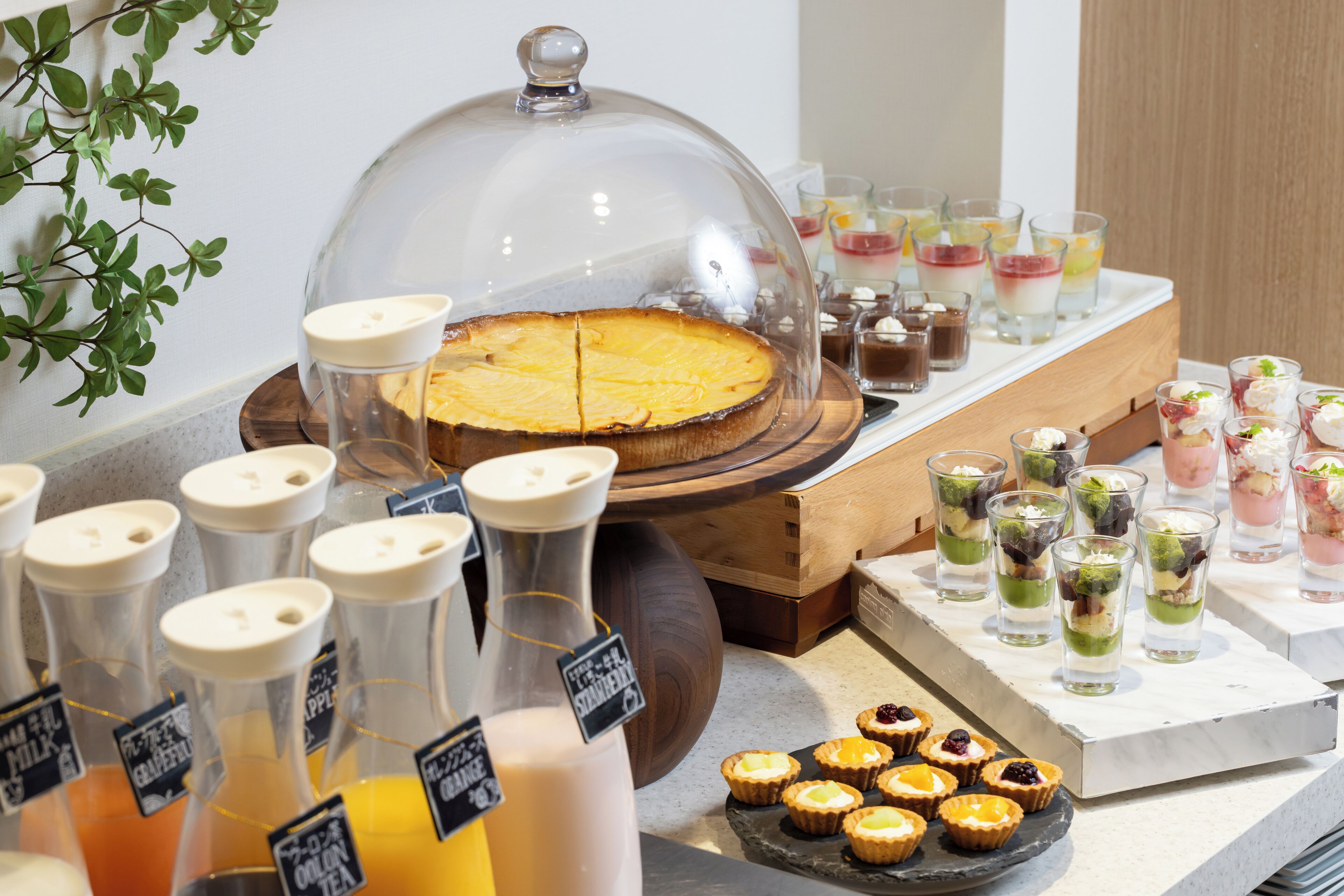 Un bufé con una variedad de alimentos, incluyendo un pastel cubierto, bebidas en dispensadores y pequeños postres en una bandeja.