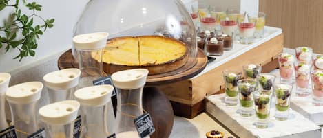 Un bufé con una variedad de alimentos, incluyendo un pastel cubierto, bebidas en dispensadores y pequeños postres en una bandeja.