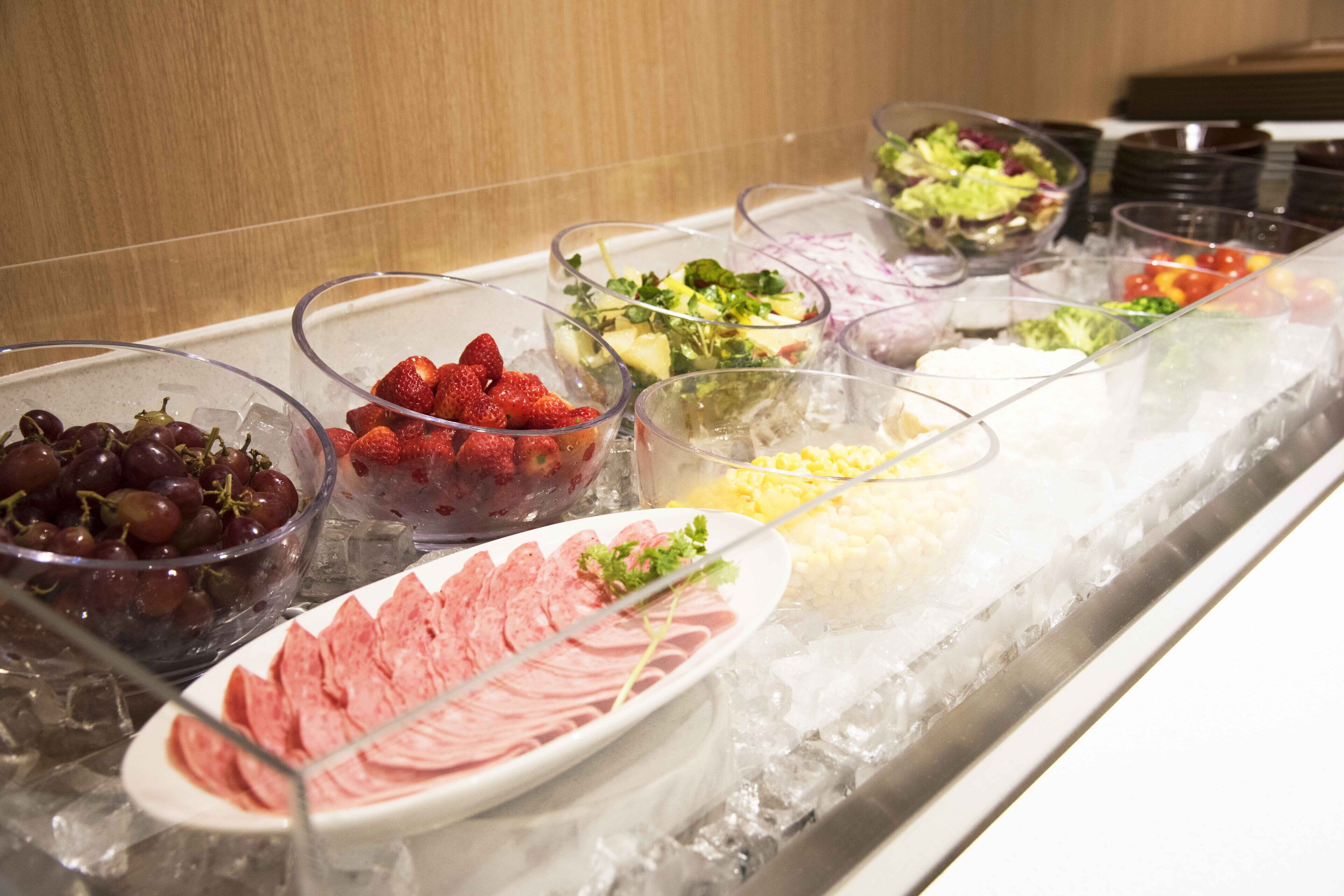 Un buffet proposant une variété de plats, notamment des raisins, des fraises, des salades et des viandes.