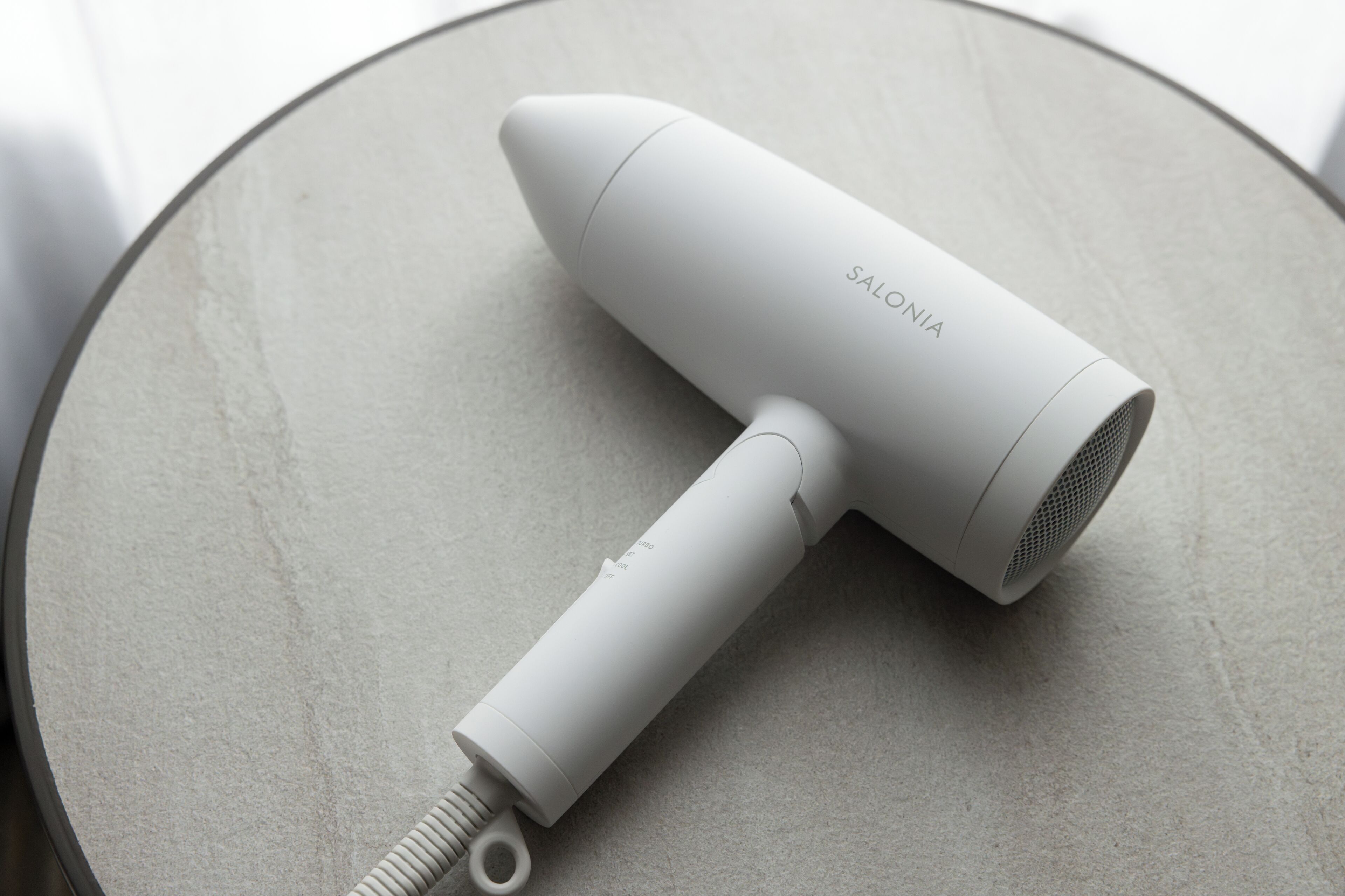 A white hair dryer with the brand name "SALONIA" on a round table.