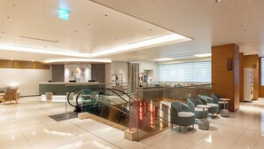 A modern hotel lobby with a glass elevator, seating area, reception desk, and a staircase. - Richmond Hotel Utsunomiya Ekimae Annex (Utsunomiya)