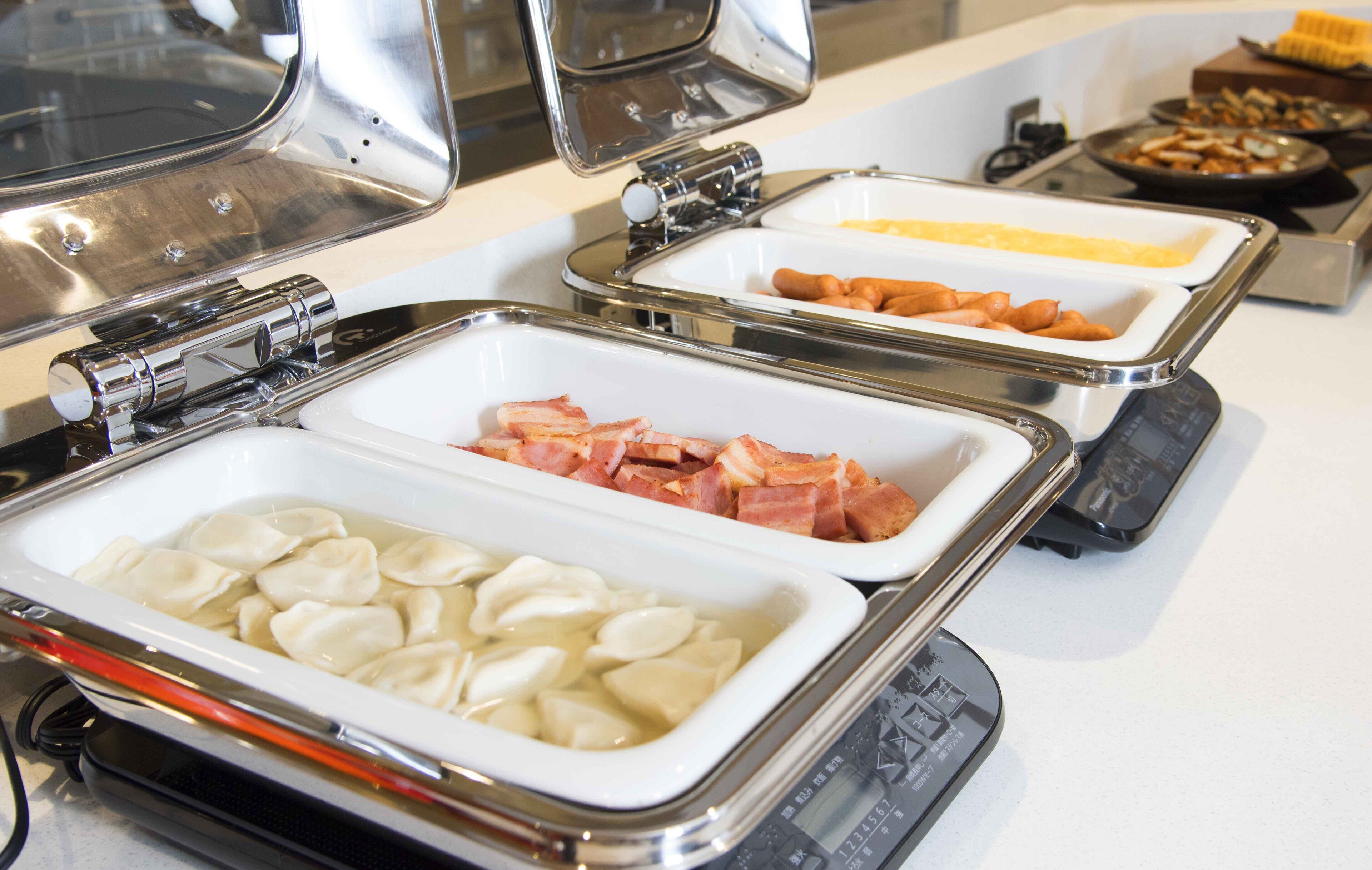 A buffet with various food items including dumplings, bacon, and sausages.