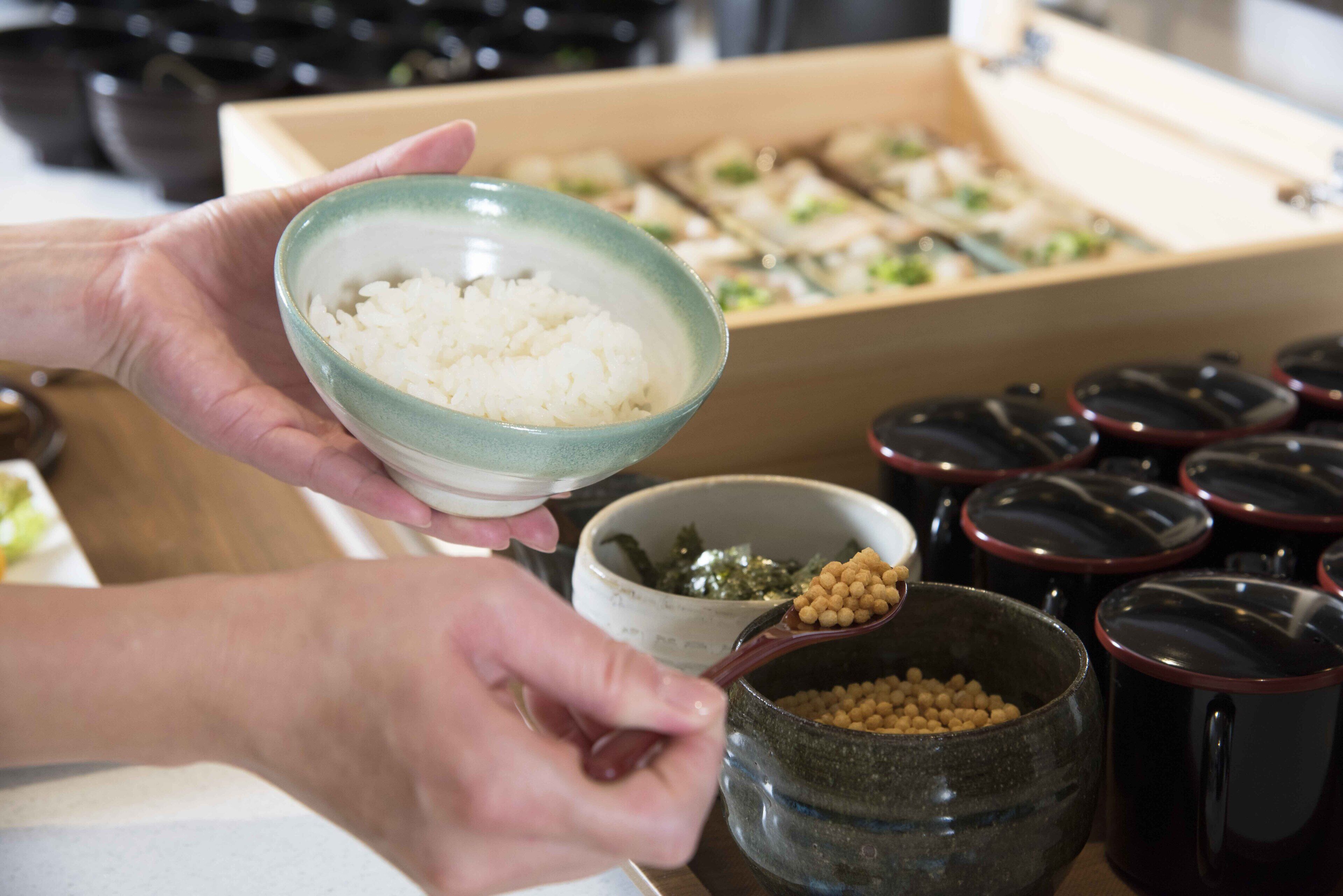 Una persona sostiene un bol de arroz, con varios pequeños platos y recipientes al fondo.