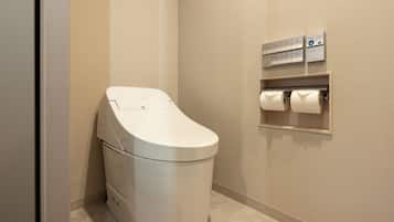 A compact, modern bathroom with a built-in washer and dryer, a toilet paper dispenser, and a shelf with additional supplies.