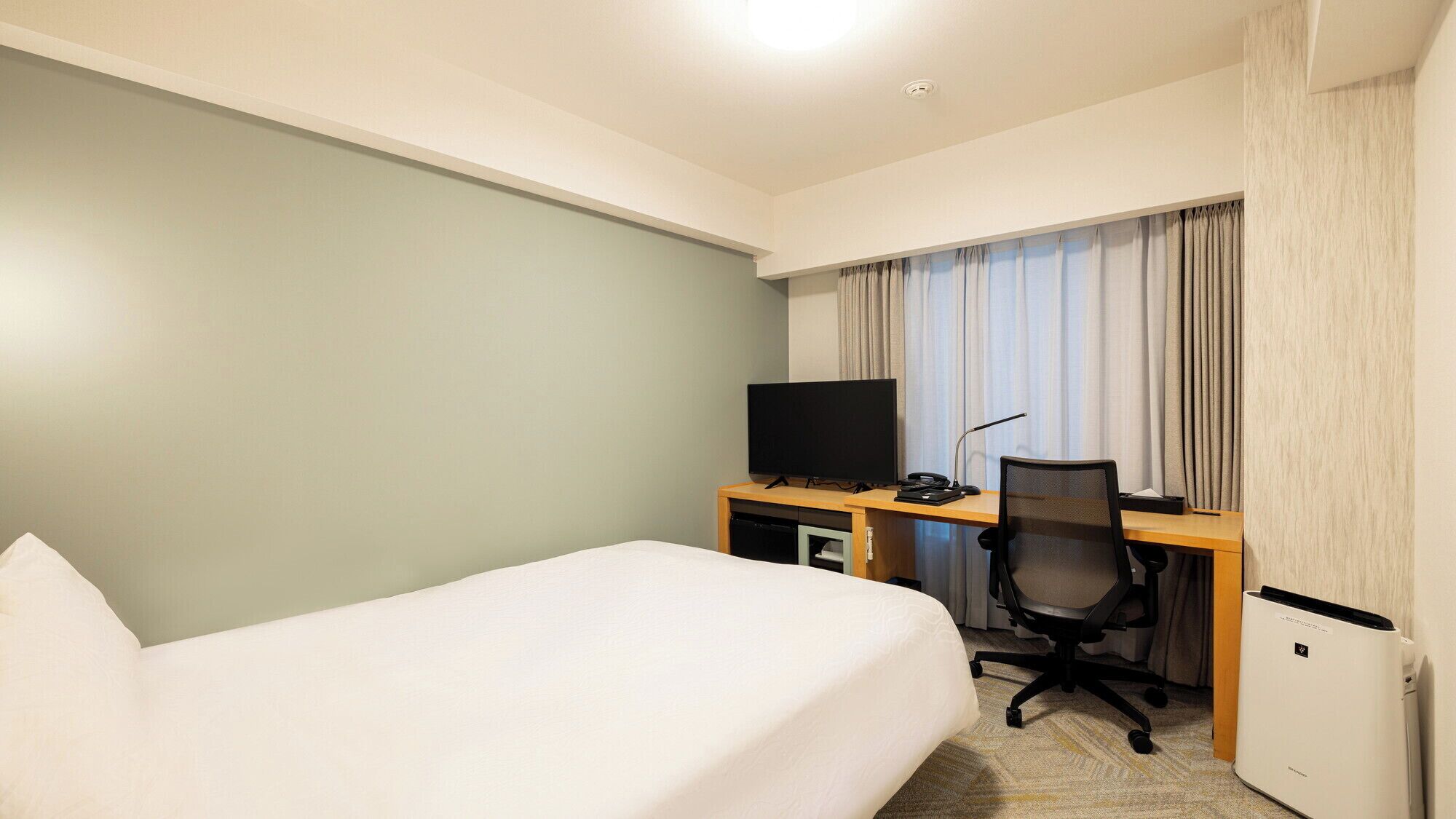 Une chambre d’hôtel équipée d’un lit, d’un bureau avec un ordinateur, d’une télévision et d’un petit climatiseur.