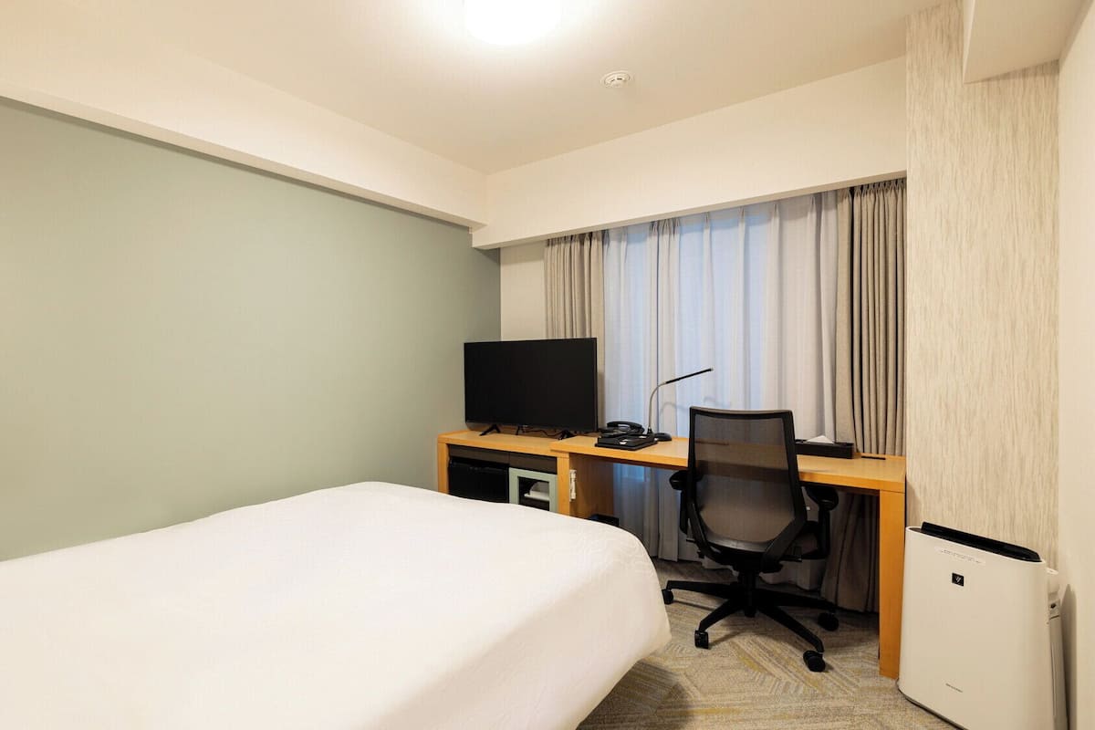 Ein Hotelzimmer mit einem Bett, einem Schreibtisch mit Computer, einem Fernseher und einer Klimaanlage.