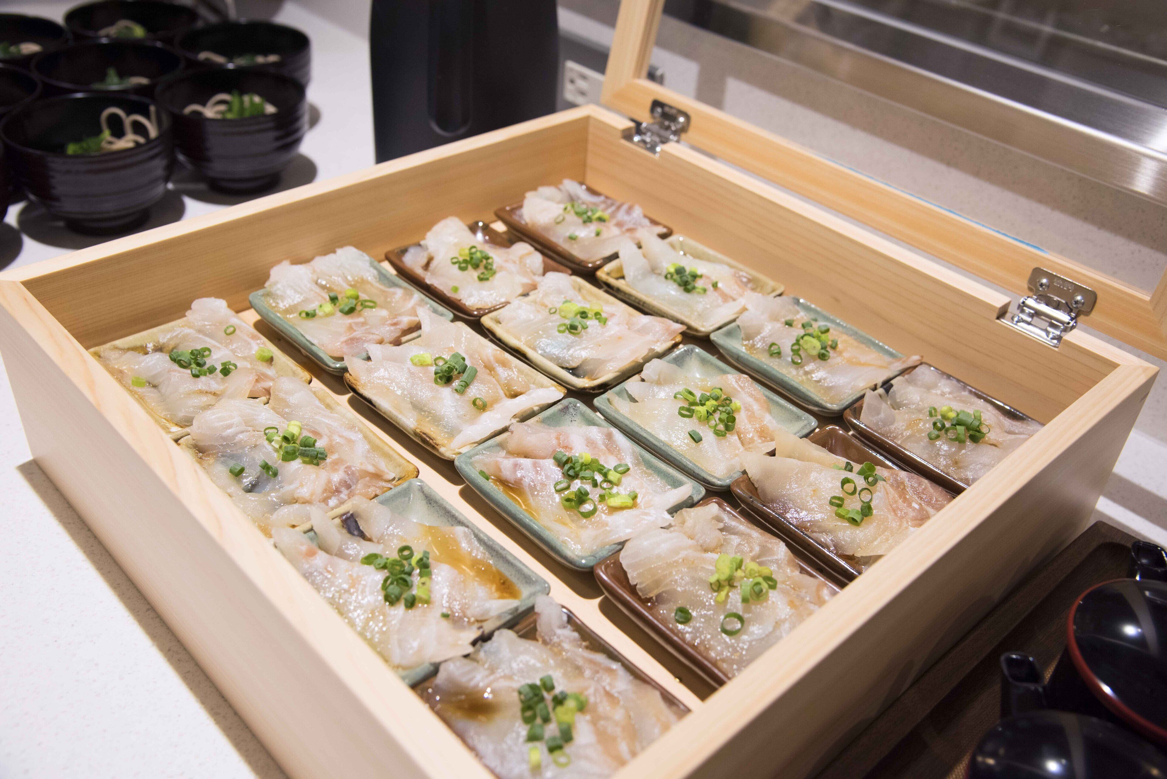 A wooden box containing neatly arranged sashimi pieces garnished with green onions.