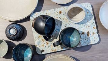A table with various ceramic dishes and cups, some with reflective surfaces, arranged on a speckled tray.