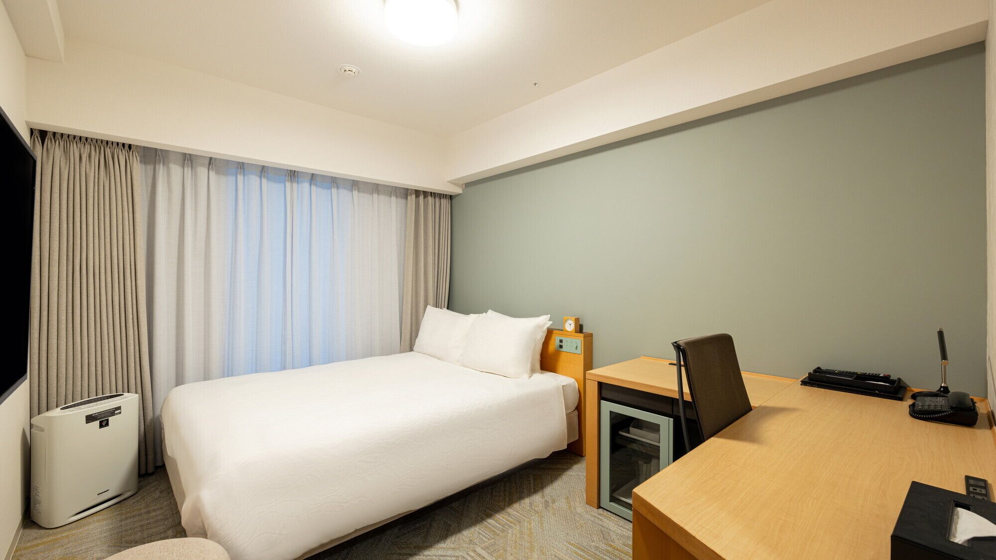 Een hotelkamer met een bed, een bureau, een stoel, een telefoon en een prullenbak.