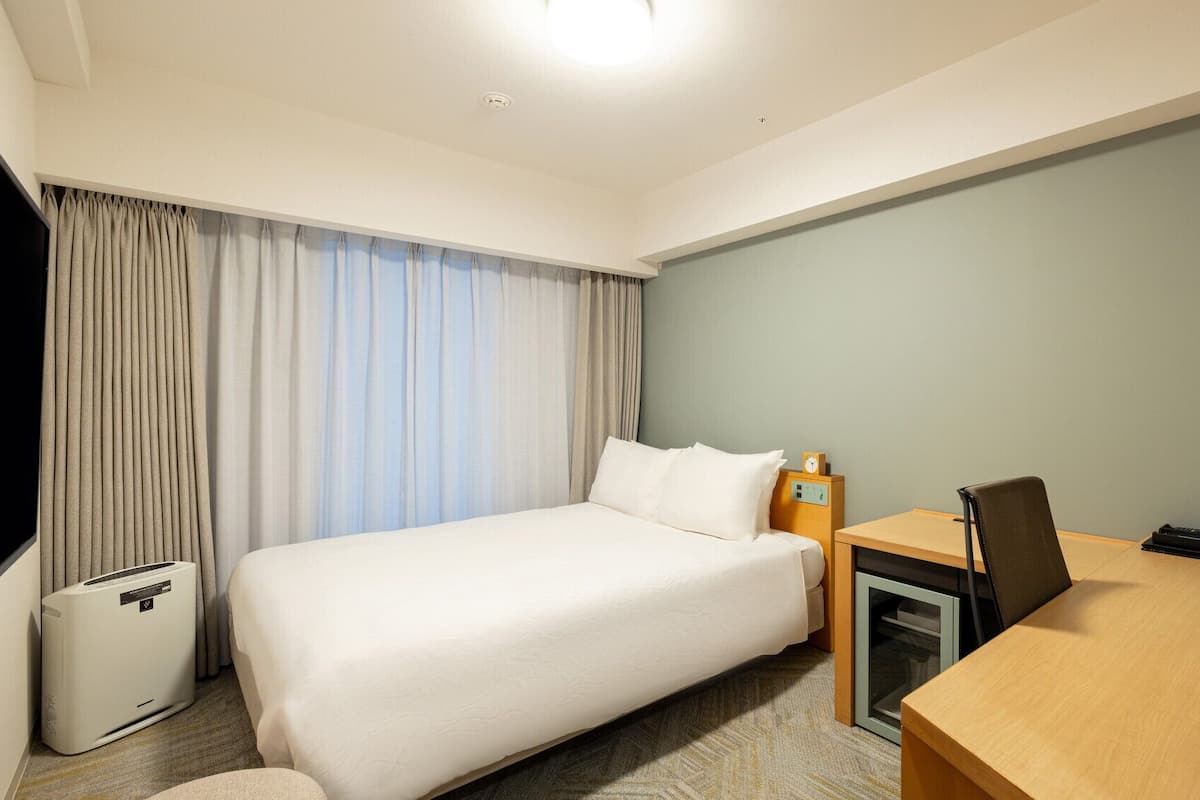 Une chambre d’hôtel équipée d’un lit, d’un bureau, d’une chaise, d’un téléphone et d’une poubelle.