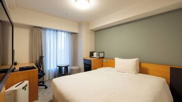 A hotel room with a large bed, a desk with a computer, a chair, a small table, and a window with curtains.