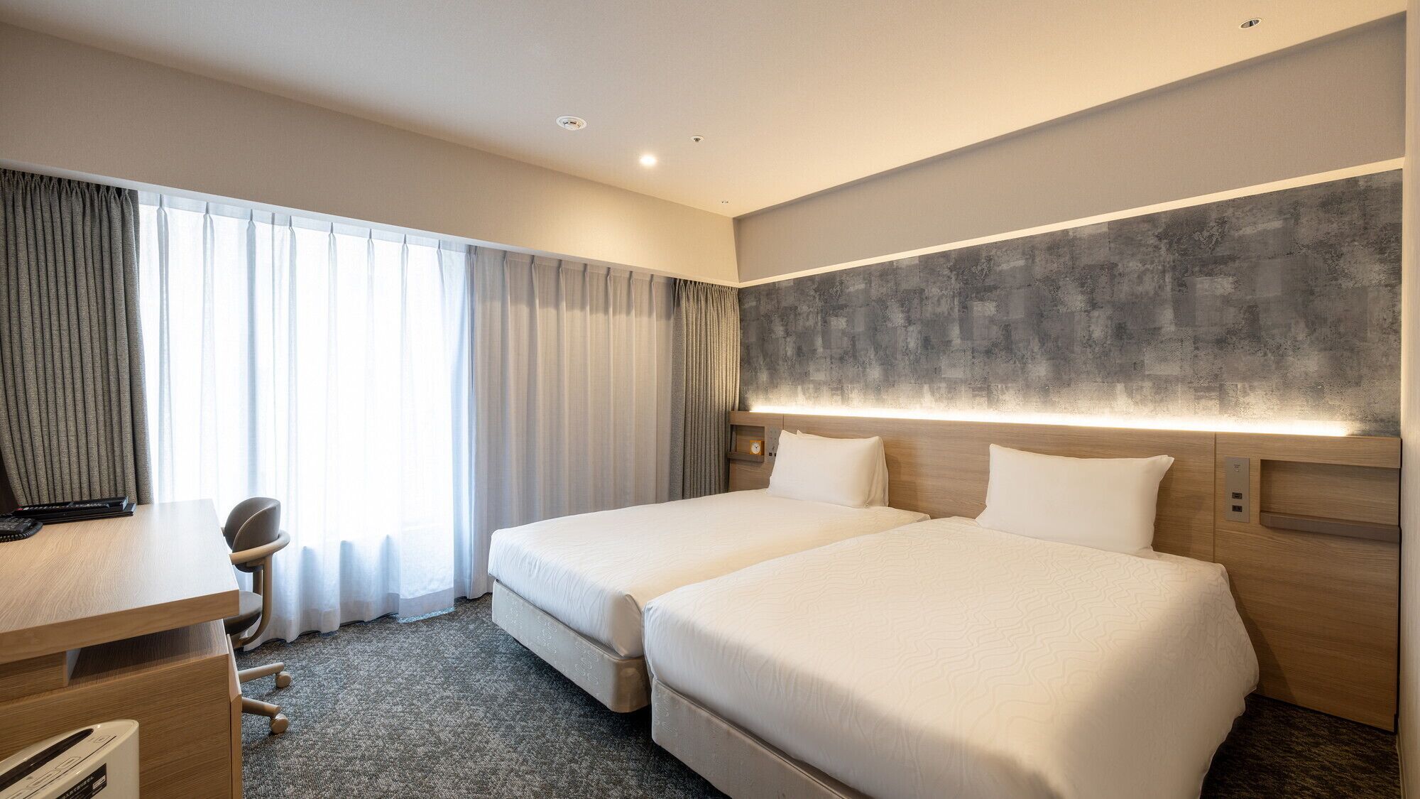 Een hotelkamer met twee bedden, een bureau, een stoel en een groot raam met gordijnen.
