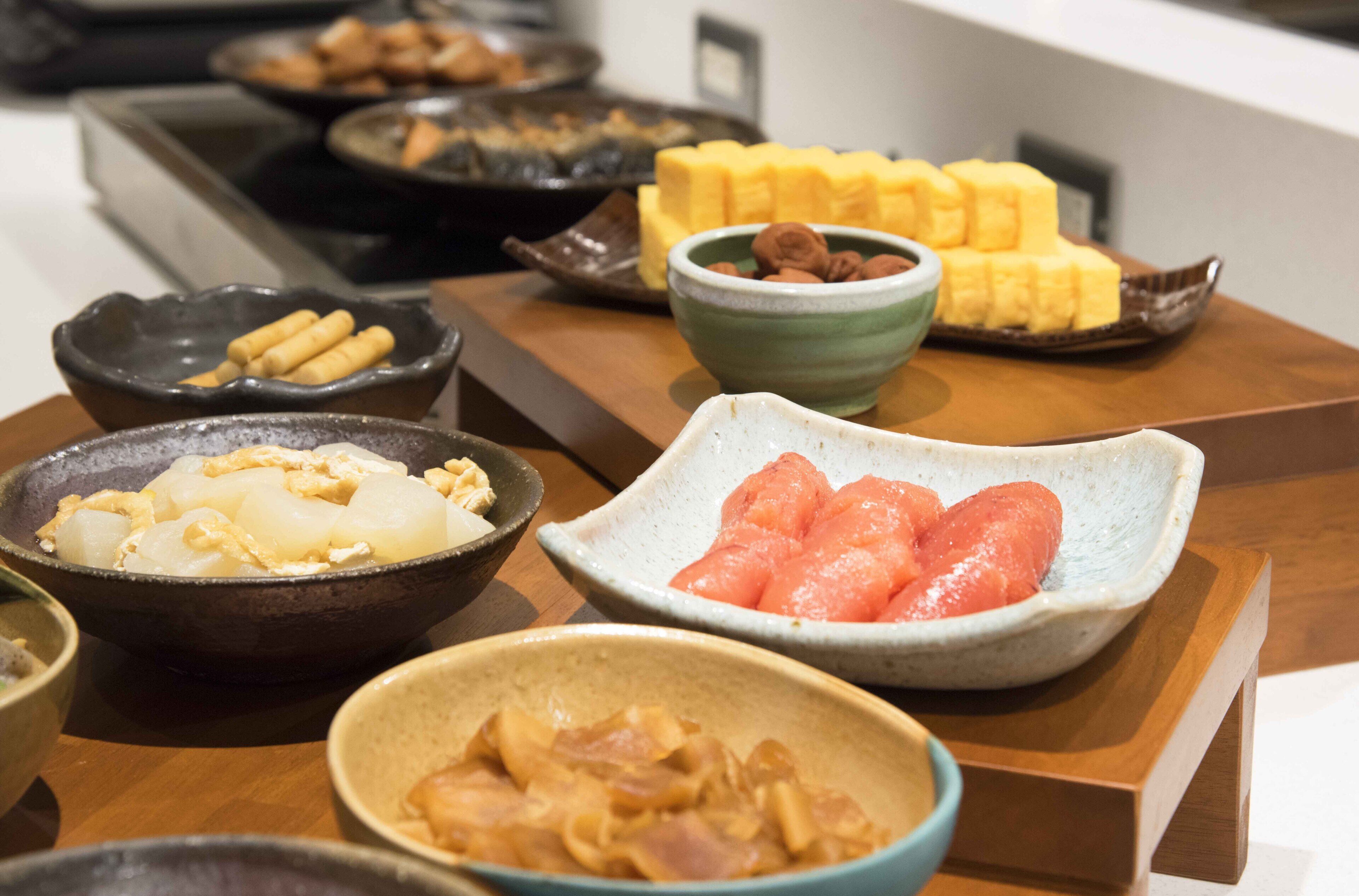 A variety of dishes on a wooden table, including what appears to be dumplings, sliced watermelon, and other food items.