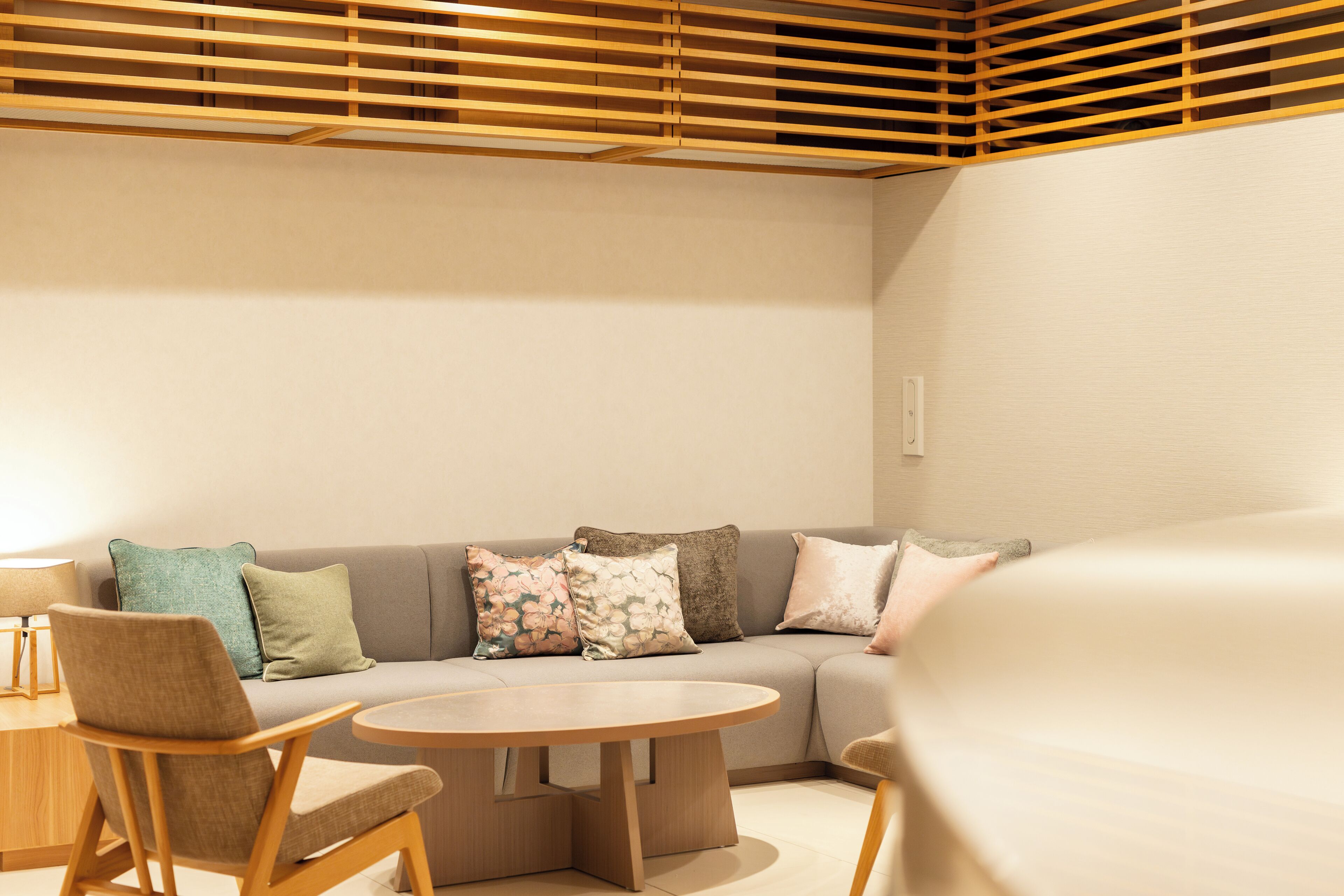 A modern living room with a sofa, two armchairs, a coffee table, and a wooden slatted ceiling.