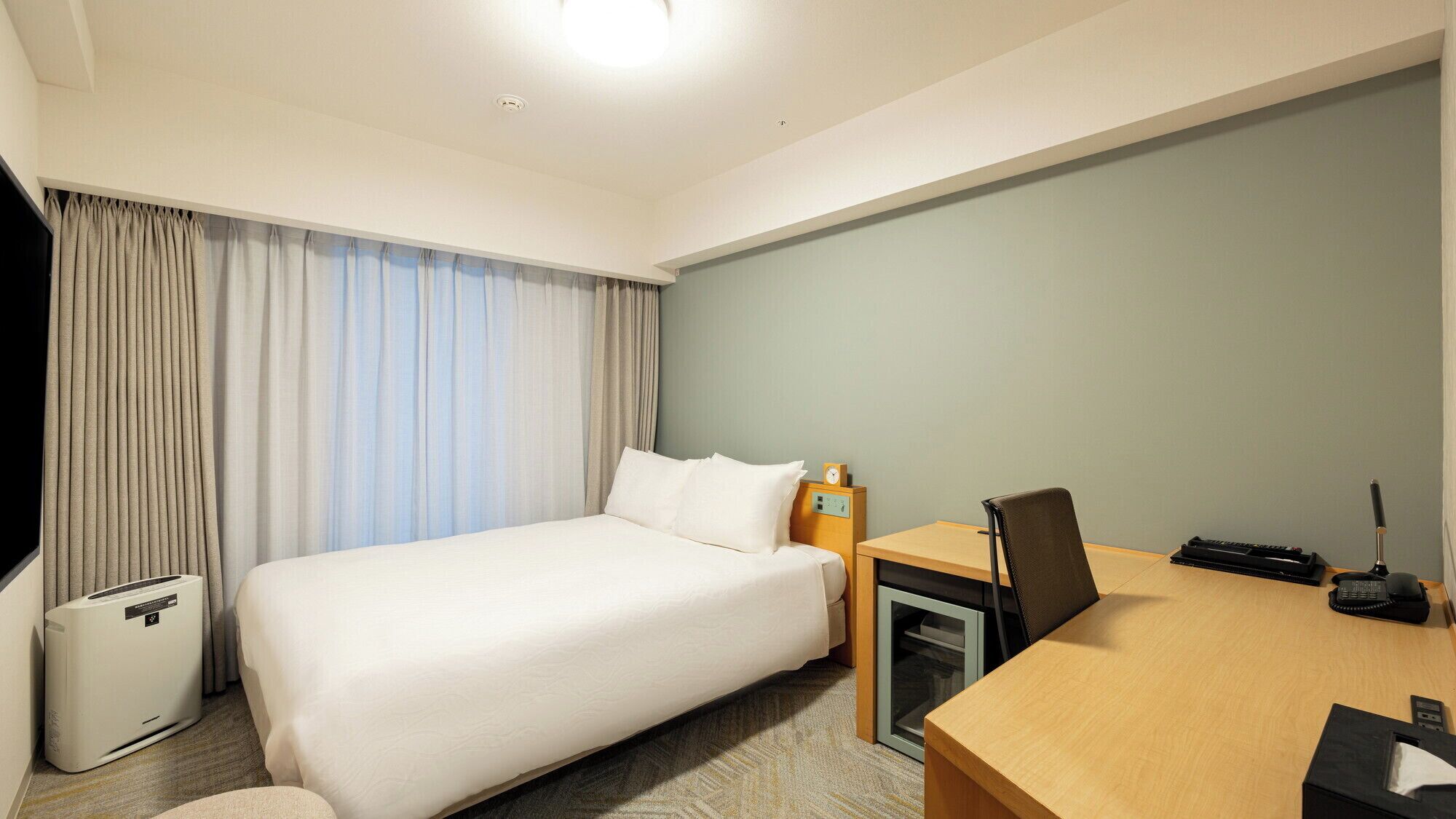 Une chambre d’hôtel avec un lit, un bureau, une chaise et une petite table avec une lampe.