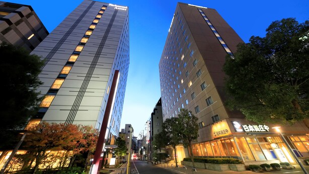 A modern hotel with a glass facade, surrounded by tall buildings and trees. - Richmond Hotel Utsunomiya Ekimae Annex (Utsunomiya)