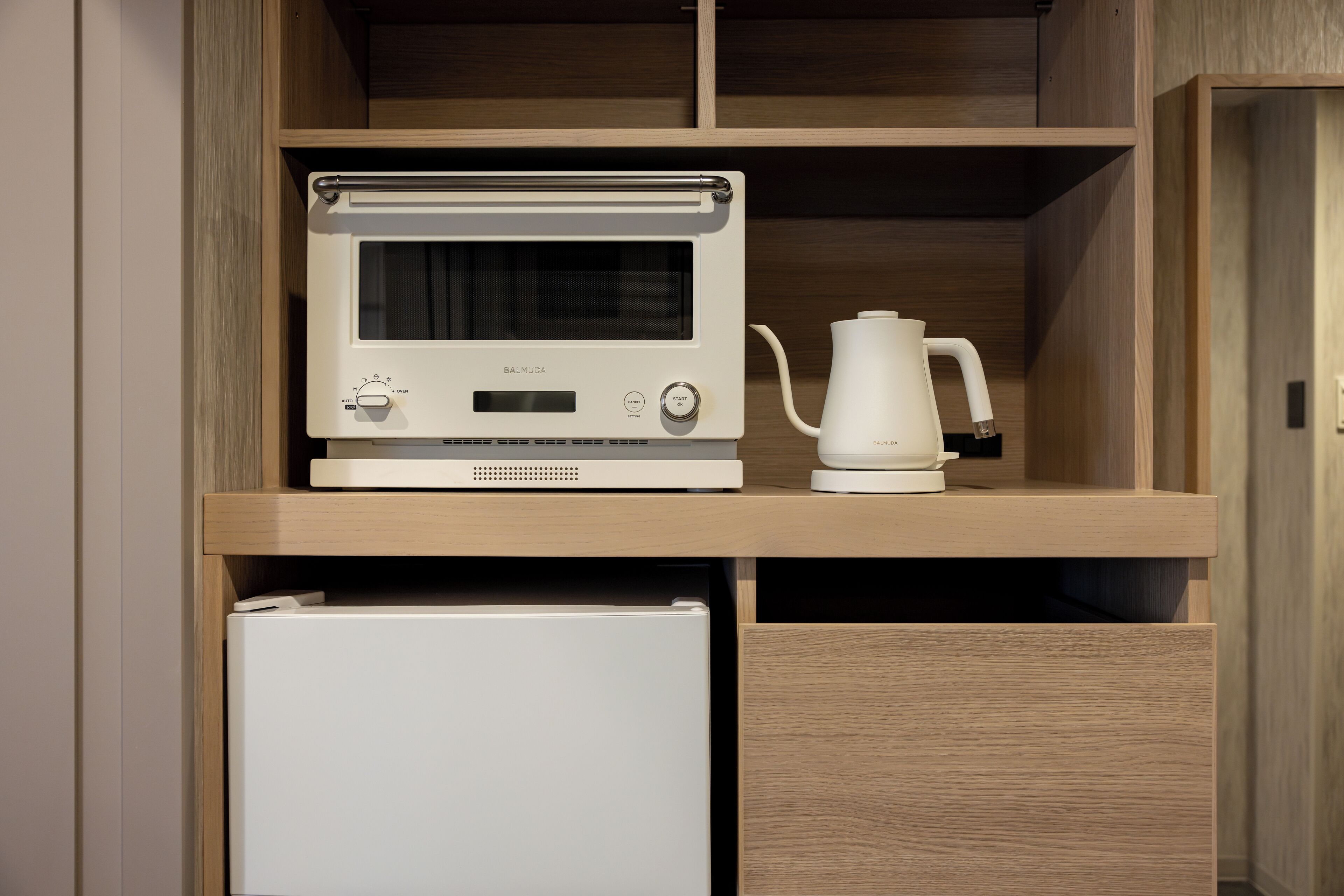 A kitchen with a microwave oven and a kettle on a wooden shelf.