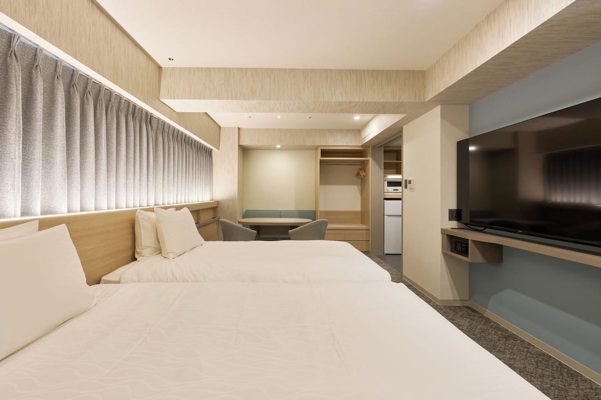 A hotel room with two beds, a TV, a small table, and a seating area.
