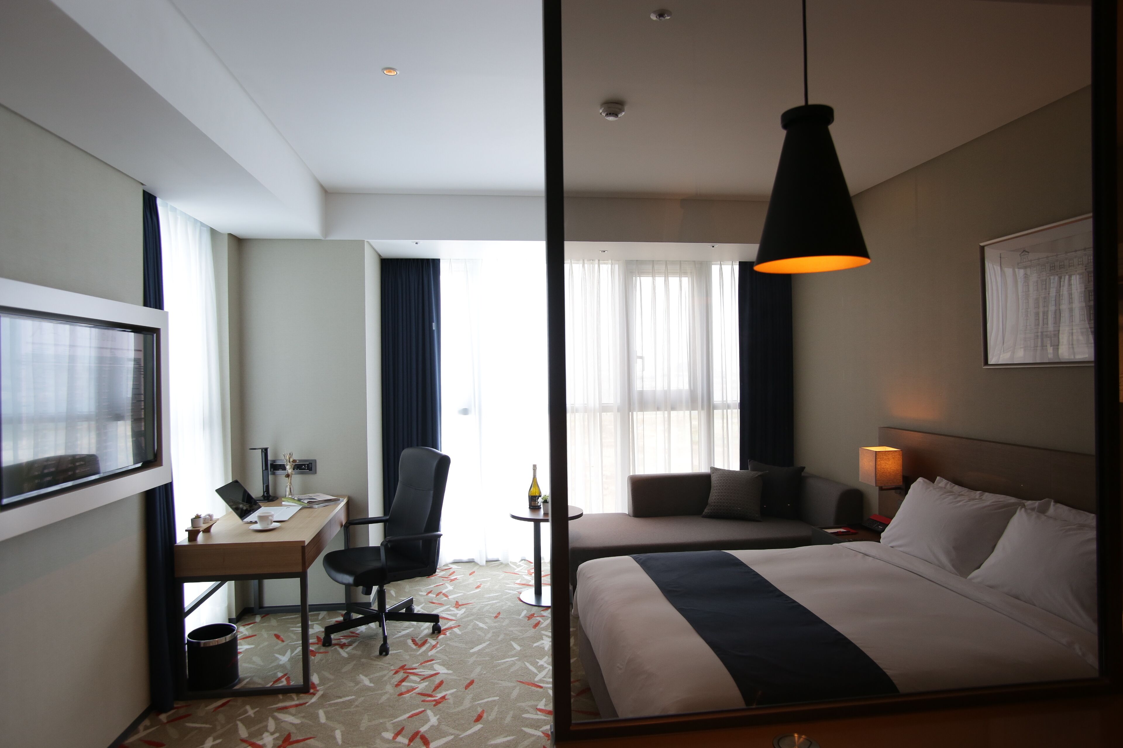 A hotel room with a bed, desk, chair, and a large window.
