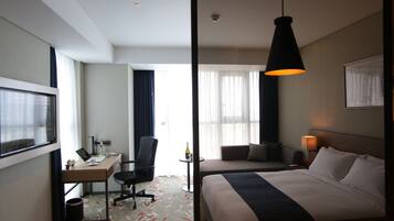A hotel room with a bed, desk, chair, and a large window.