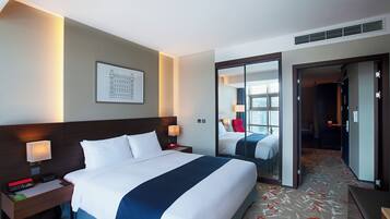 Habitación de hotel con una cama grande, mesitas de noche, un espejo y vistas a la ciudad a través de la ventana.