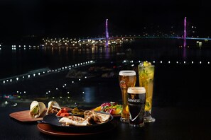 A table with food and drinks, a view of a bridge, and city lights in the background. - Asti Hotel Busan Station (Busan)