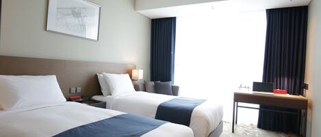 A hotel room with two beds, a desk, a chair, a lamp, and a framed picture on the wall.