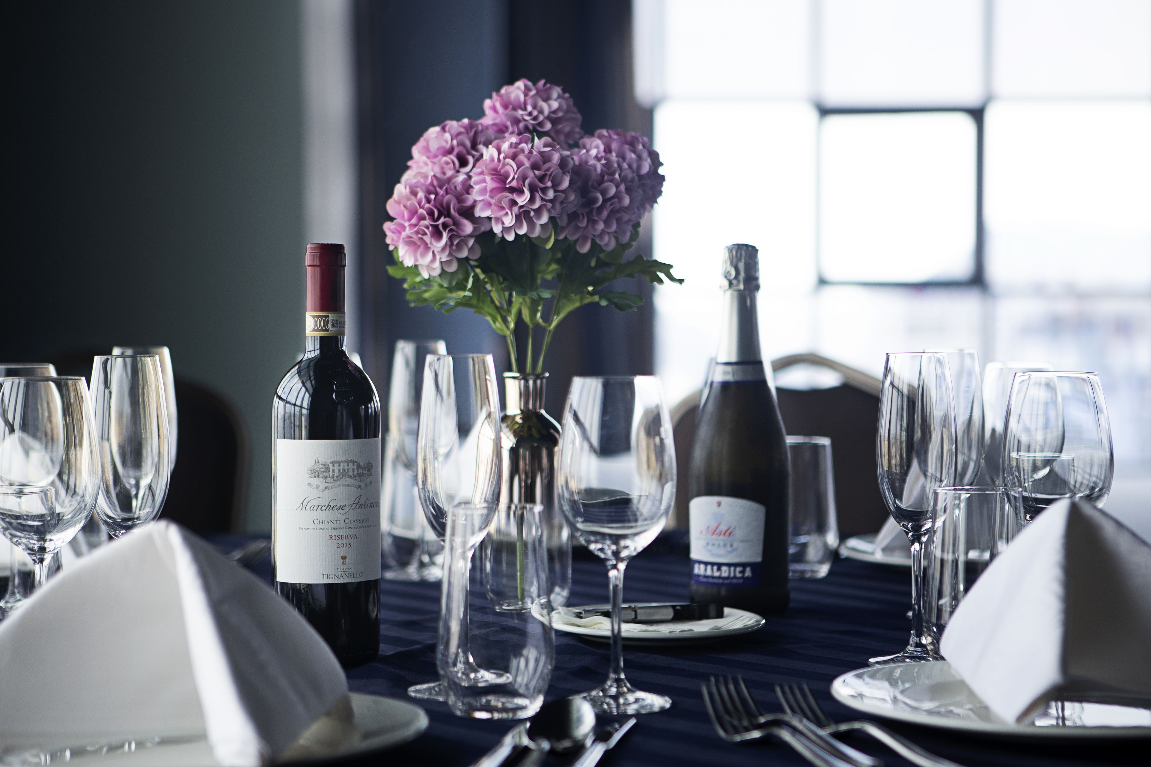 A table set for dining with wine bottles, glasses, and a vase of flowers.