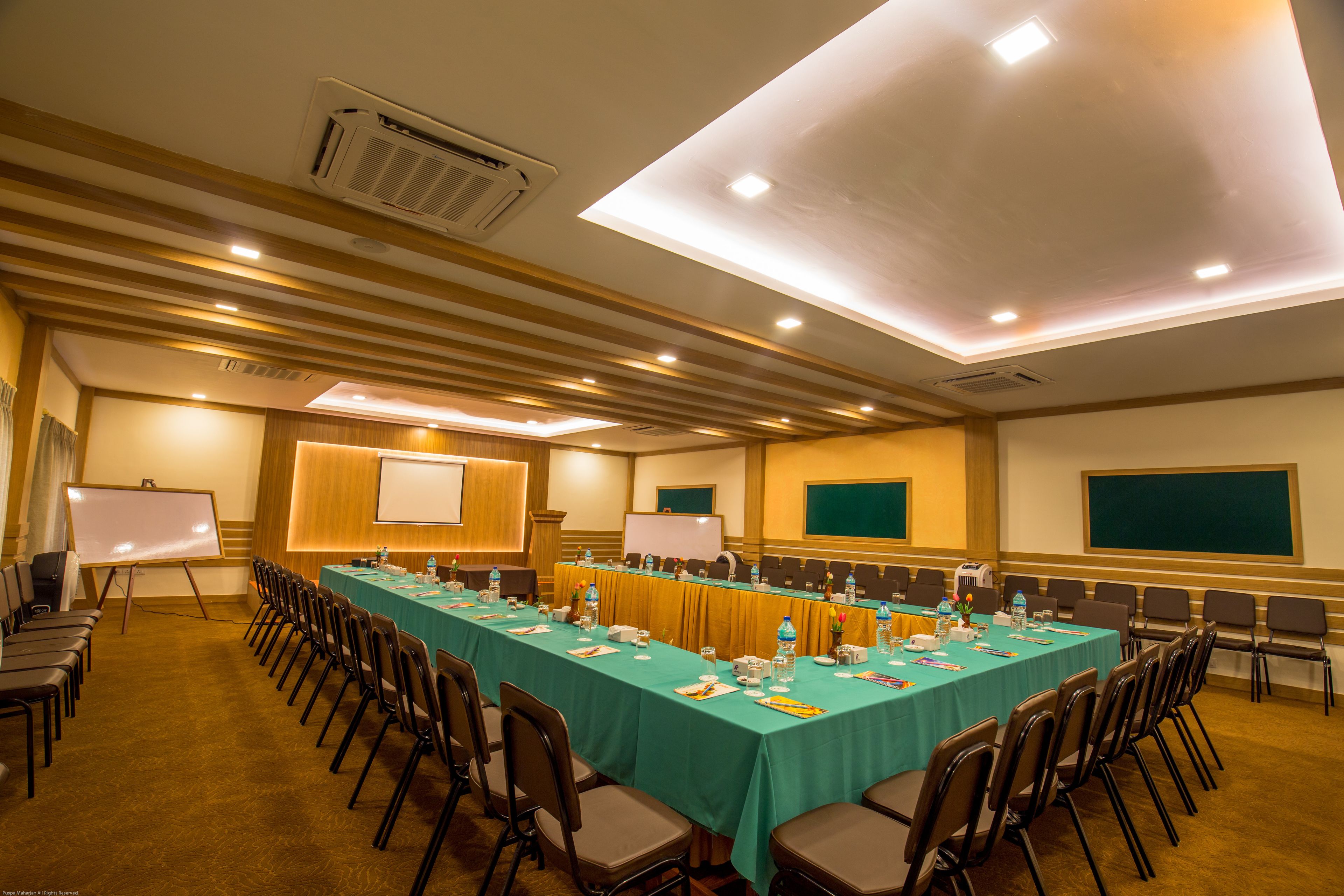 A conference room with a long table, chairs, a whiteboard, and a projector screen.