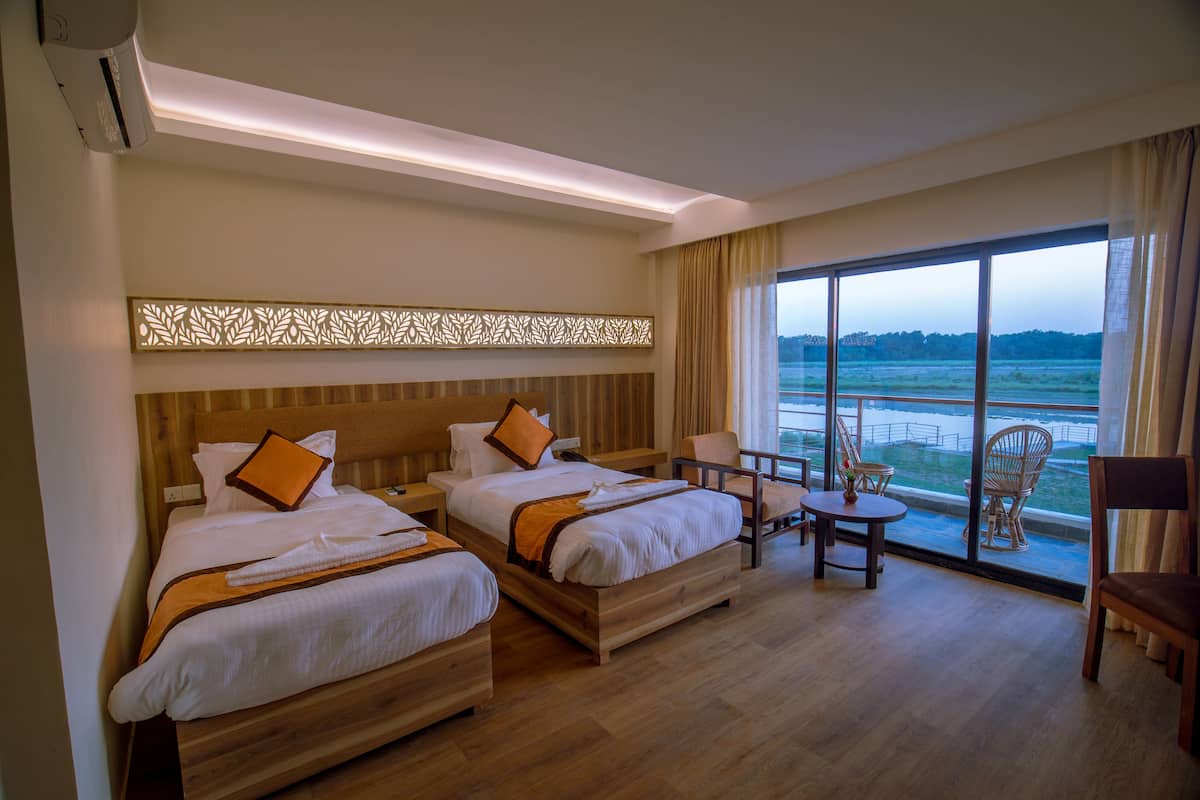 A hotel room with two beds, a balcony with chairs, and a view of the sea.