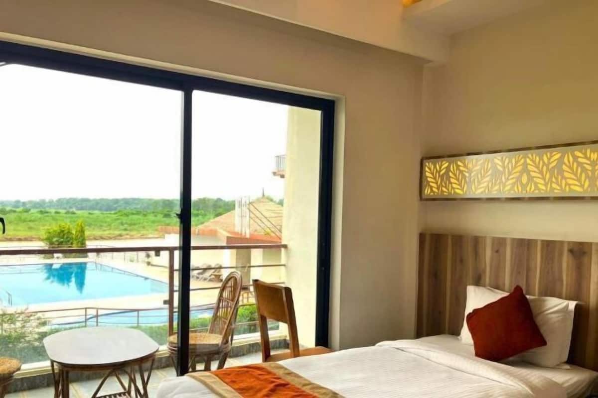 A hotel room with a large window, a bed, a small table, and a chair.