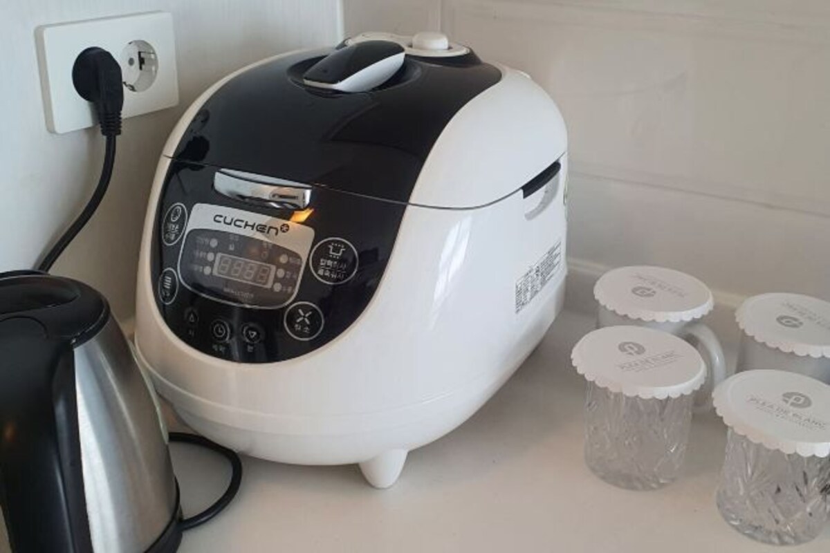 A white and black CUCHAN rice cooker with a digital display, connected to a power outlet.