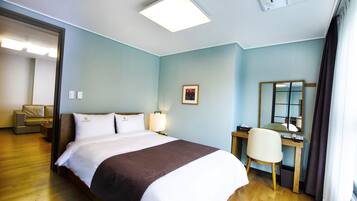 A hotel room with a bed, a desk, a chair, a desk lamp, a framed picture, and a window with curtains.
