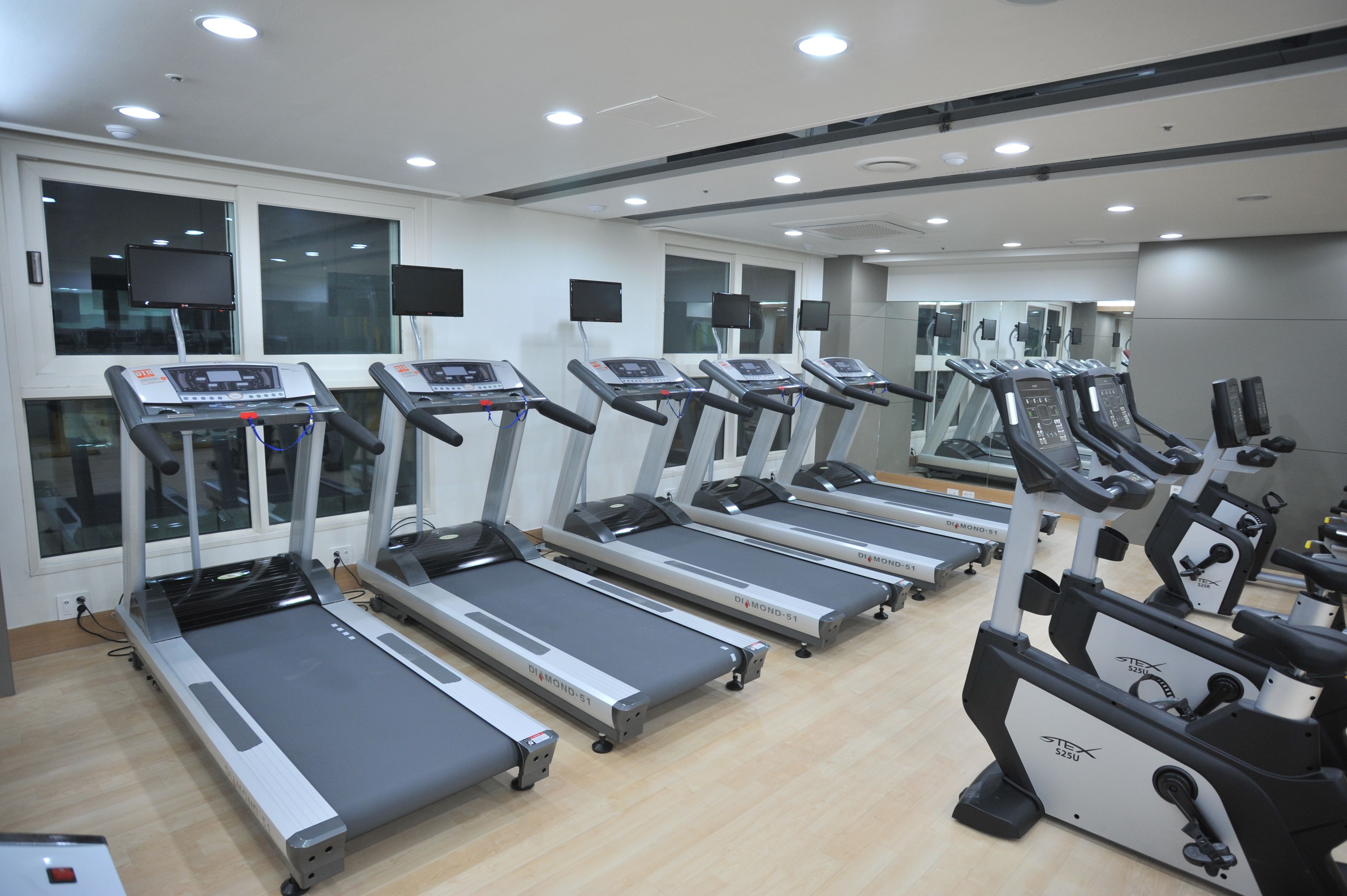 A gym with multiple treadmills and exercise bikes, large windows, and a clean, modern design.