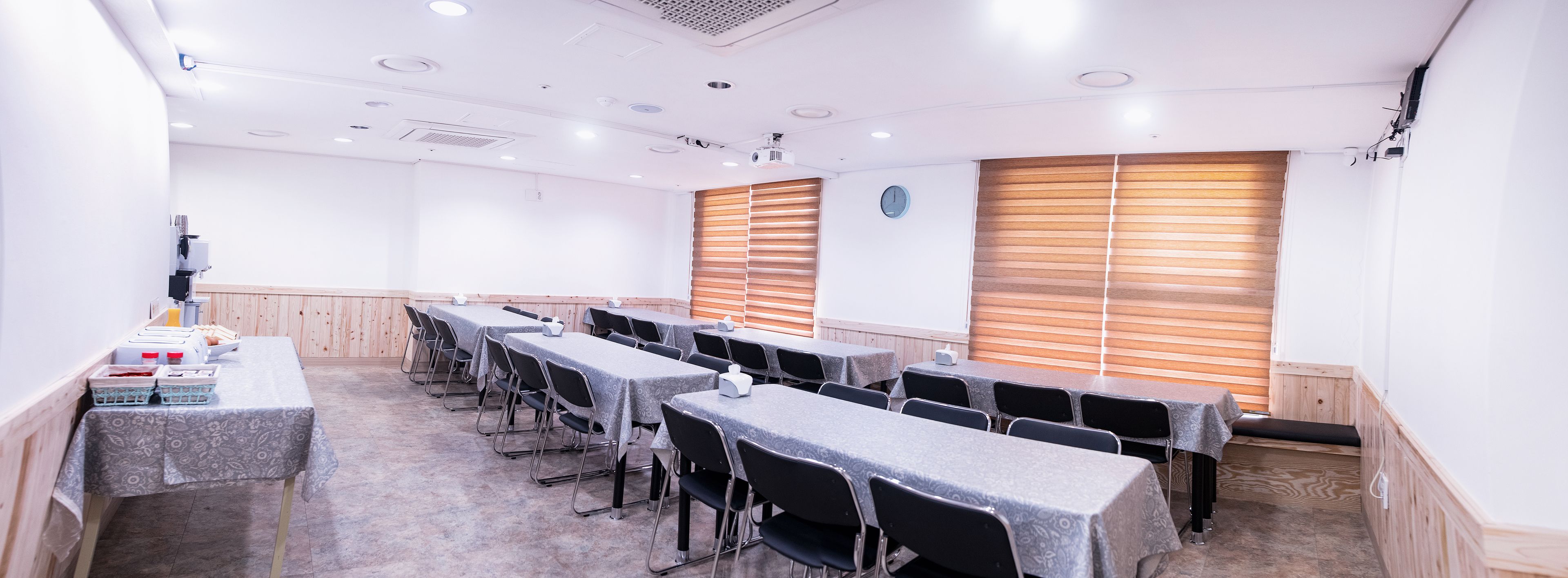Un salón de conferencias con mesas largas, sillas negras y paneles de madera en las paredes.