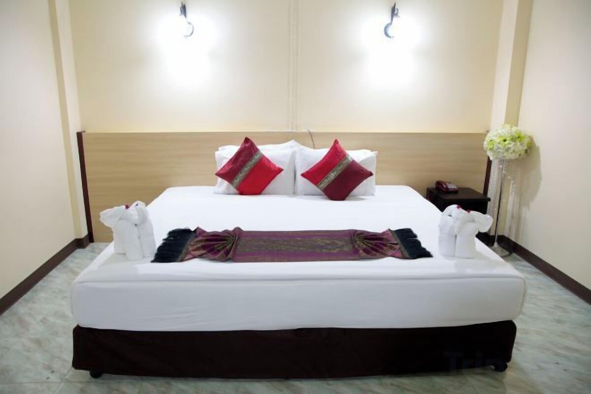 A neatly made bed with white linens, red and green pillows, and a decorative headboard.
