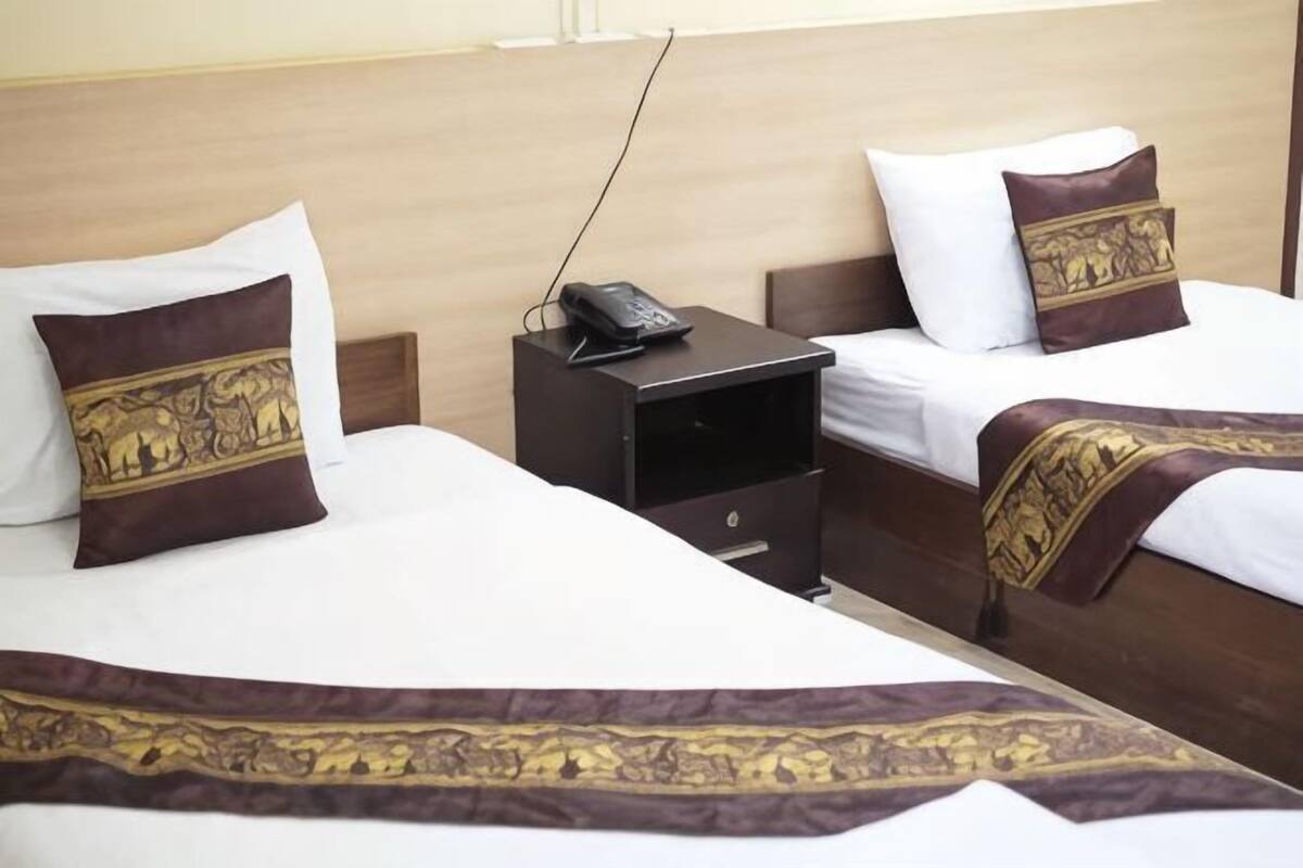 Ein Hotelzimmer mit zwei Betten, jeweils mit Kissen und Decke. Ein Nachttisch mit Telefon und Schublade ist vorhanden.