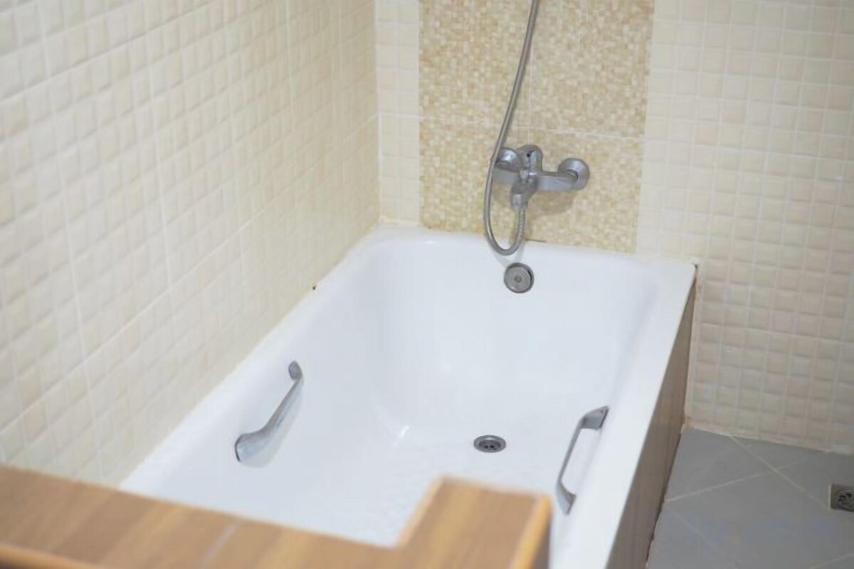 Een badkamer met een witte badkuip, een douchekop en een betegelde wand.