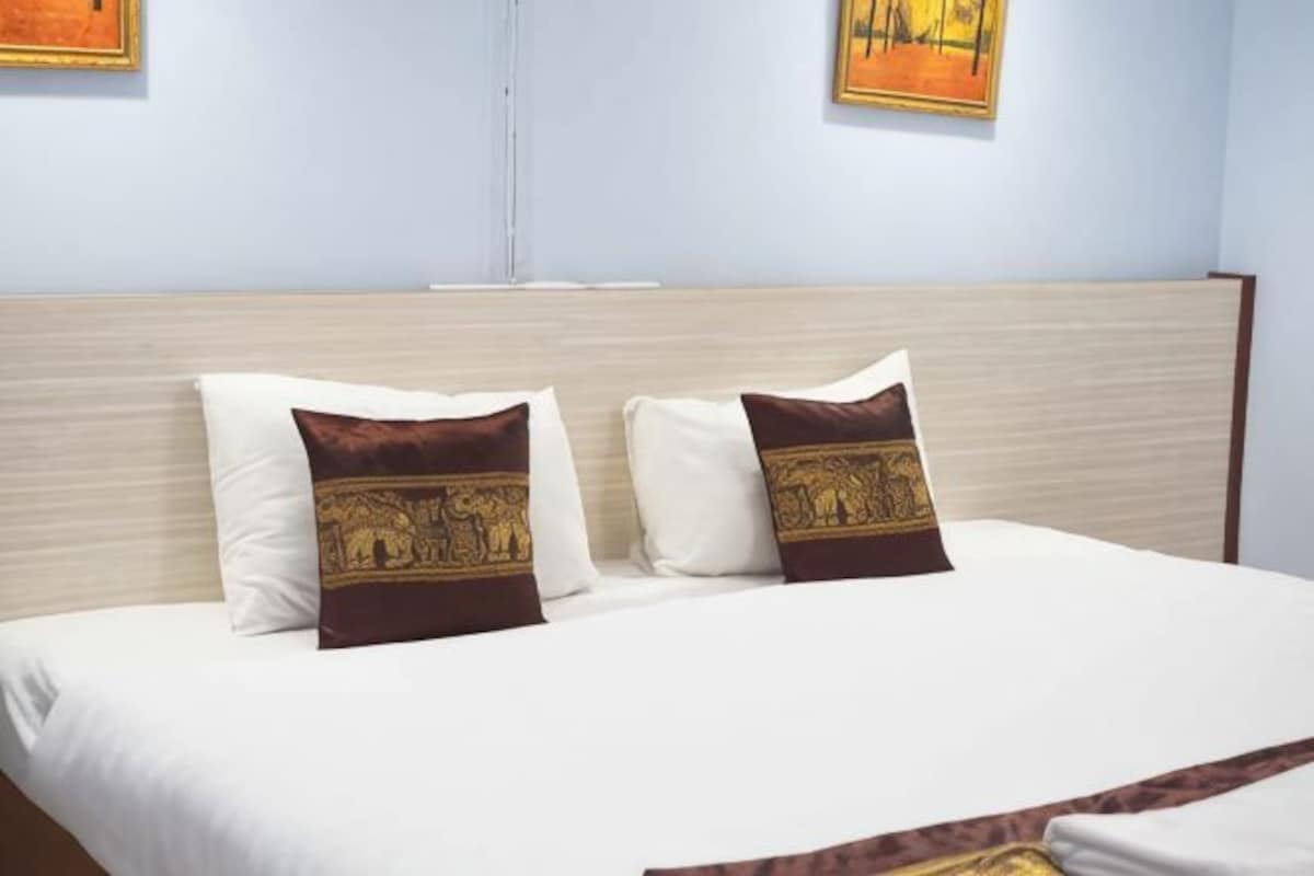 A neatly made bed with two pillows, a headboard, and two framed pictures on the wall.