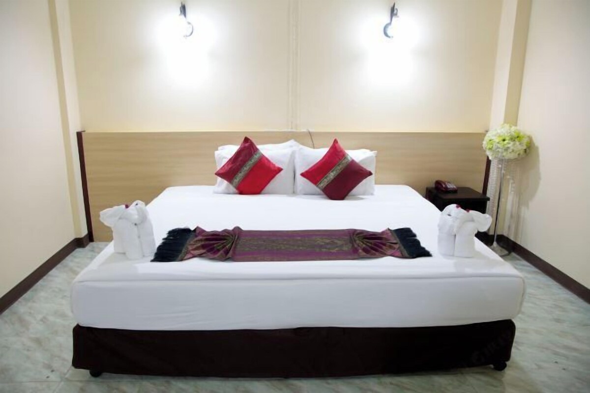 A hotel room with a large bed, two bedside tables, a nightstand, and a wall-mounted lamp.