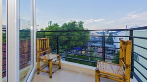 A balcony with two wooden chairs, a glass door, and a view of buildings and trees.