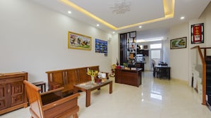 A spacious living room with a wooden sofa, a coffee table, and a dining area with a table and chairs. - Hoi An Green Town House Homestay (Da Nang)